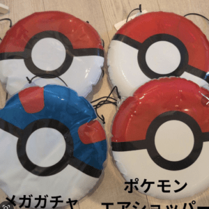 Four Poké Ball balloons (red, white, black ring) laid on a wooden floor; one shows a blue section and a bit of text overlay.  Articulos Japan (Post Box Japan)