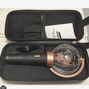 Open zip case with a black handheld microphone featuring copper accents and a glass sphere, plus a user manual inside.