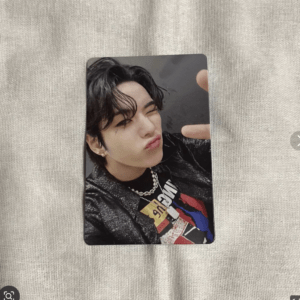 Close-up portrait photo card of a person with black hair, winking and puckering lips, wearing a black glittery jacket, graphic tee, and pearl necklace.