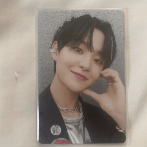 Portrait photo card of a smiling young man with black hair, wearing a blazer and layered silver chains, hand near his face.