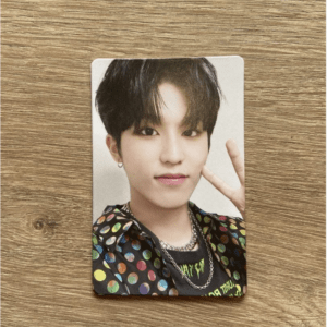 Photo card showing a young man with short black hair, wearing a multicolored polka-dot jacket and a silver chain, making a peace sign with his right hand.