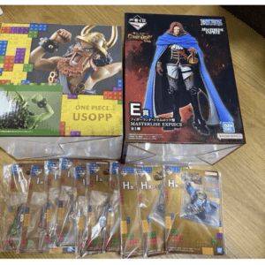 Two boxed figure sets on a wooden floor: One Piece USOPP box on the left and Masterlise ExPiece box on the right, with sealed collectible card packs in front.