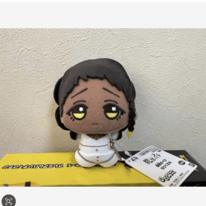 Soft plush doll of a young character with black hair, huge yellow eyes, wearing a white outfit, sitting on a yellow surface with a tag nearby.