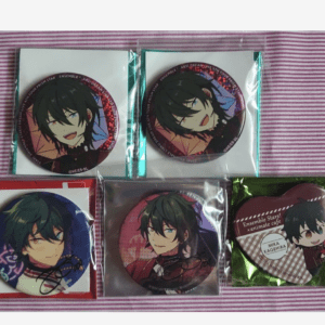 Five anime badges on a pink striped surface: two round buttons at the top in clear packaging, and three badges below (left blue-toned circle, middle red-toned circle, right heart-shaped badge with text).